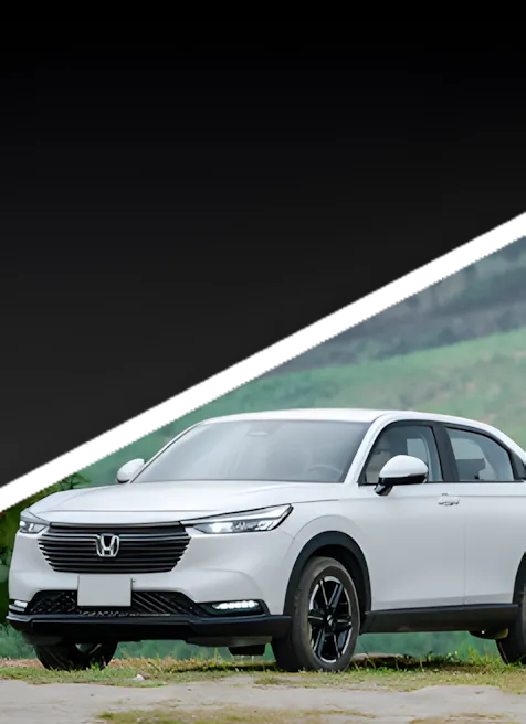A white Honda SUV is parked outdoors on a grassy area, with rolling green hills in the background and a black diagonal overlay at the top of the image.