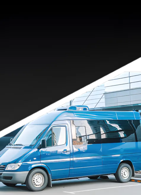 A blue passenger van is parked in front of a modern glass building, viewed from the side. The background fades to black in the upper part of the image.