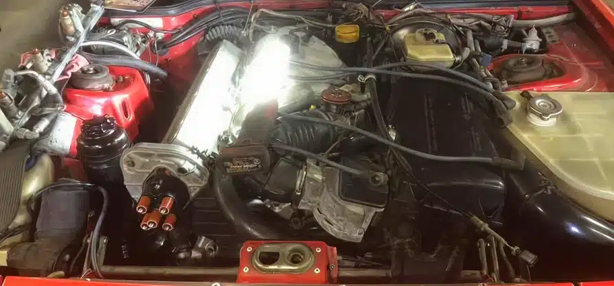 Engine service & repair in Grawn, MI at Integrity Import Service. View of a car engine bay showing various engine components, hoses, and wires. The engine parts are arranged within a red-painted vehicle frame, and theres a noticeable bright reflection near the center.