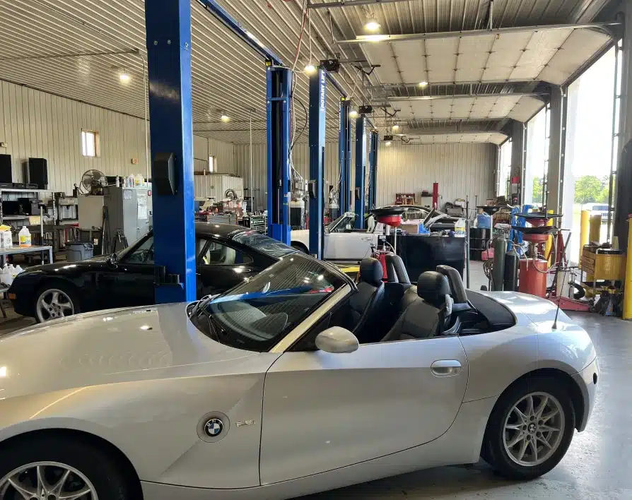 Auto repair warranty in Grawn, MI at Integrity Import Service. A white BMW convertible is parked inside a spacious auto repair shop with high ceilings, blue vehicle lifts, and various tools and equipment visible in the background.