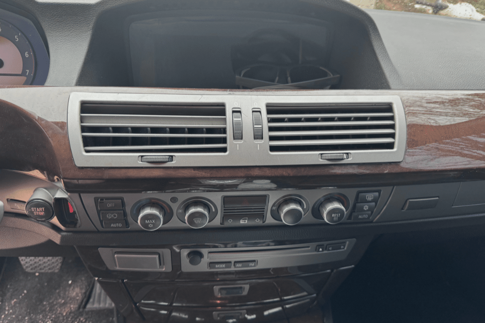 Car A/C Repair in Grawn, MI, at Integrity Import Service. A close-up of a car's dashboard featuring the central air conditioning vents and climate control panel with wood trim, highlighting components checked during an A/C repair.